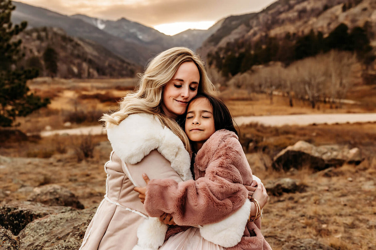 Mom hugging her school aged daughter at sunset in the mountains.