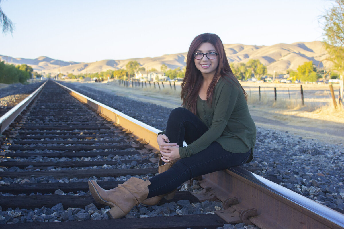 young lady sitting on golden sunlight Railroad tracks with hills in background