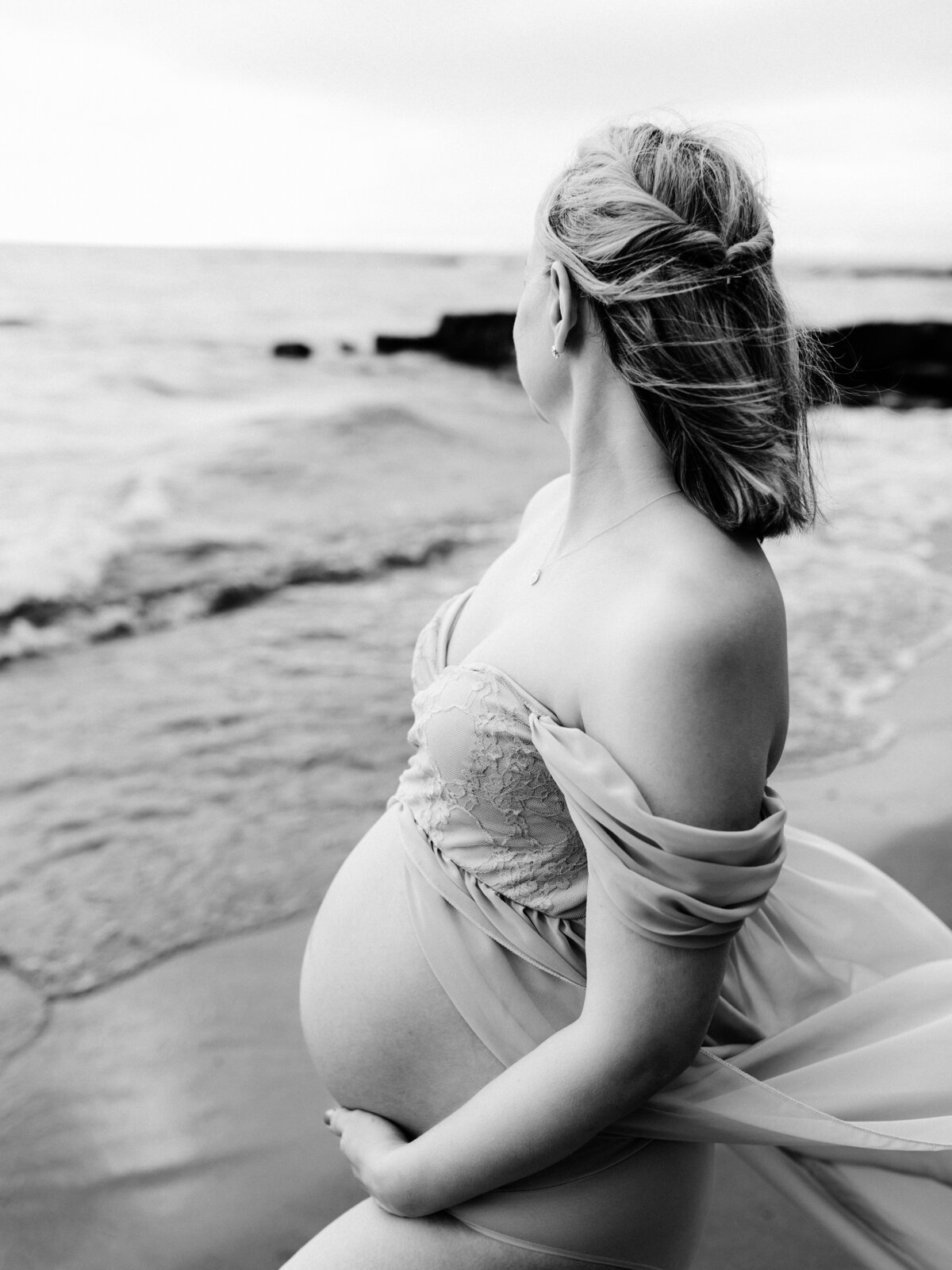 pregnant mother in purple maternity gown holding baby bump on beach for maternity photoshoot 