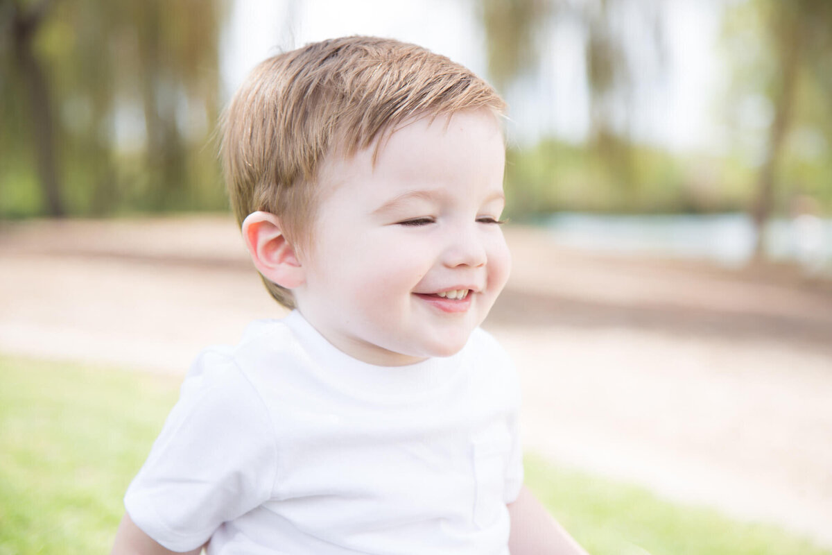 toddler boy in a white shirt laughing at the park