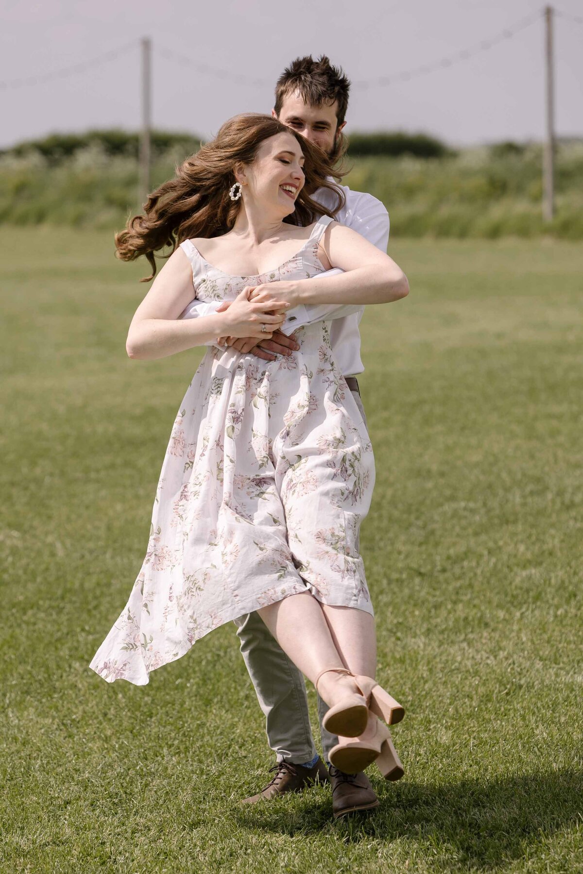 An engaged couple playing in a meadow