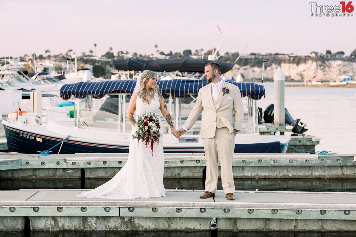 Bride and Groom stand on the docks of the bay holding hands and looking at each other