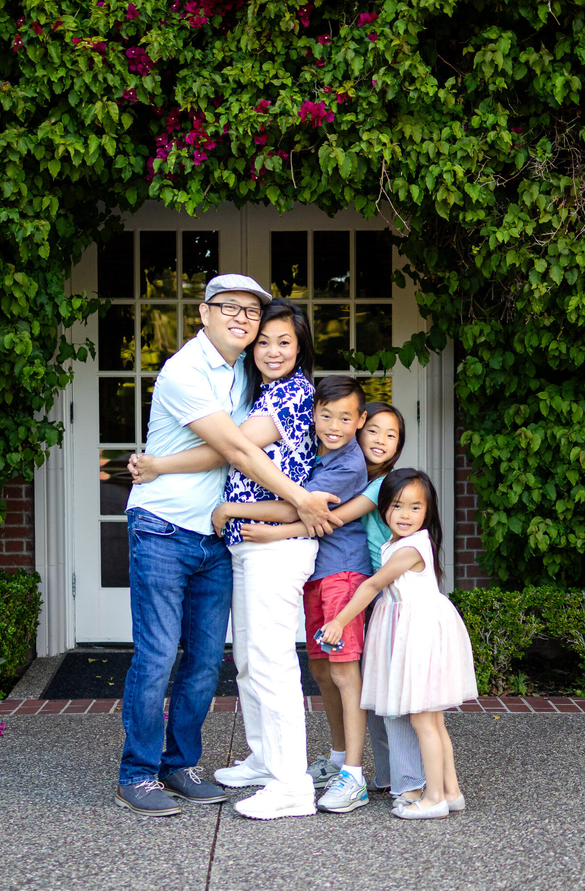 Full family hug under lush green vines and pink flowers outside their front door – Bay Area Family Portfolio - Ellobelle Photography