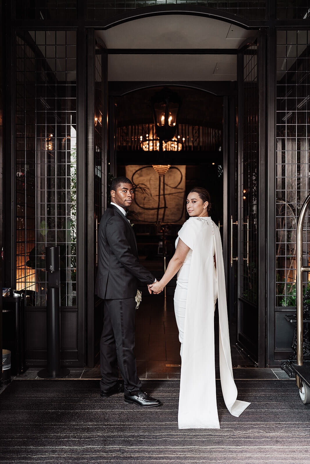 bride and groom hold hands in the entrance of the nomad hotel london as they turn and look back before arriving at their intimate wedding party