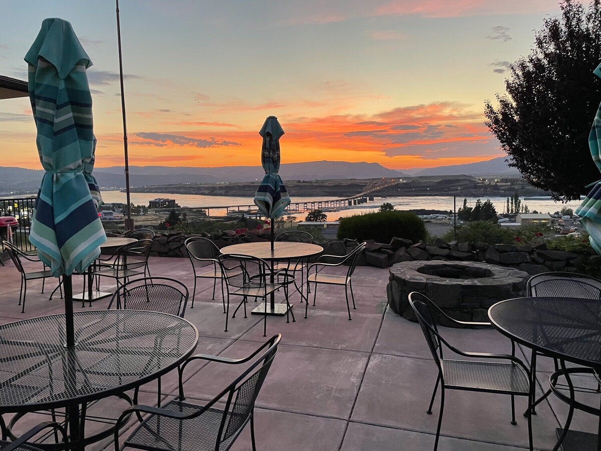 Tables with folded umbrellas, and chairs at Celilo Inn