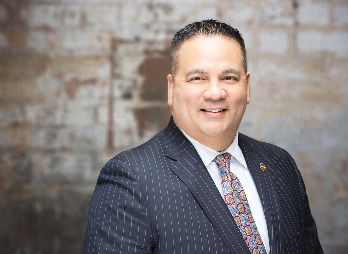 A male mortgage professional in a pin stripe suit poses for a professional corporate headshot photo on a brick wall background at Janel Lee Photography studios in Cincinnati Ohio