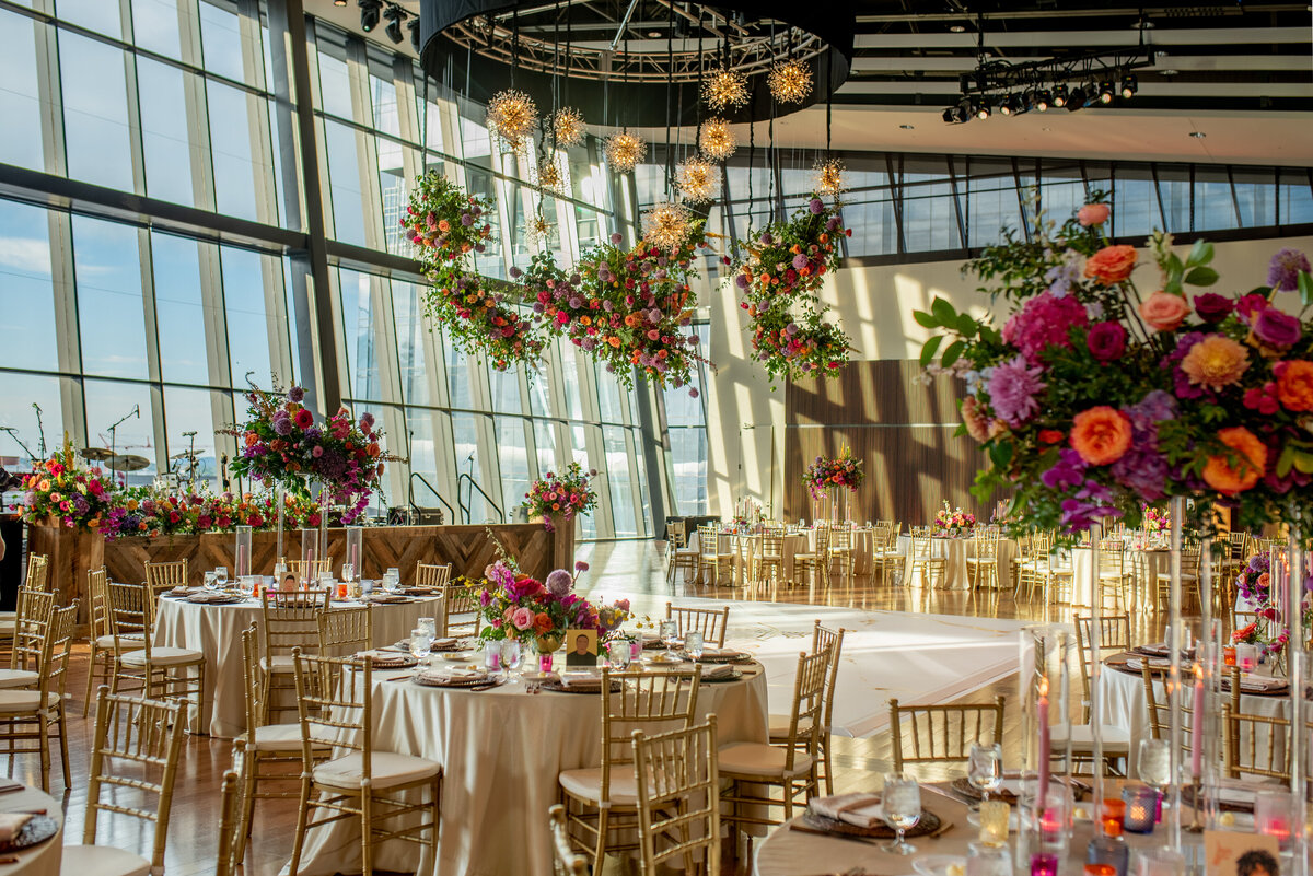 Cheerful sunset inspired summer wedding composed of petal heavy roses, garden roses, allium, orchids, ranunculus, eremurus, delphinium, and natural greenery creating hues of rosy pink, fuchsia, lavender, orange, and golden-yellow. Design by Rosemary and Finch in Nashville, TN.