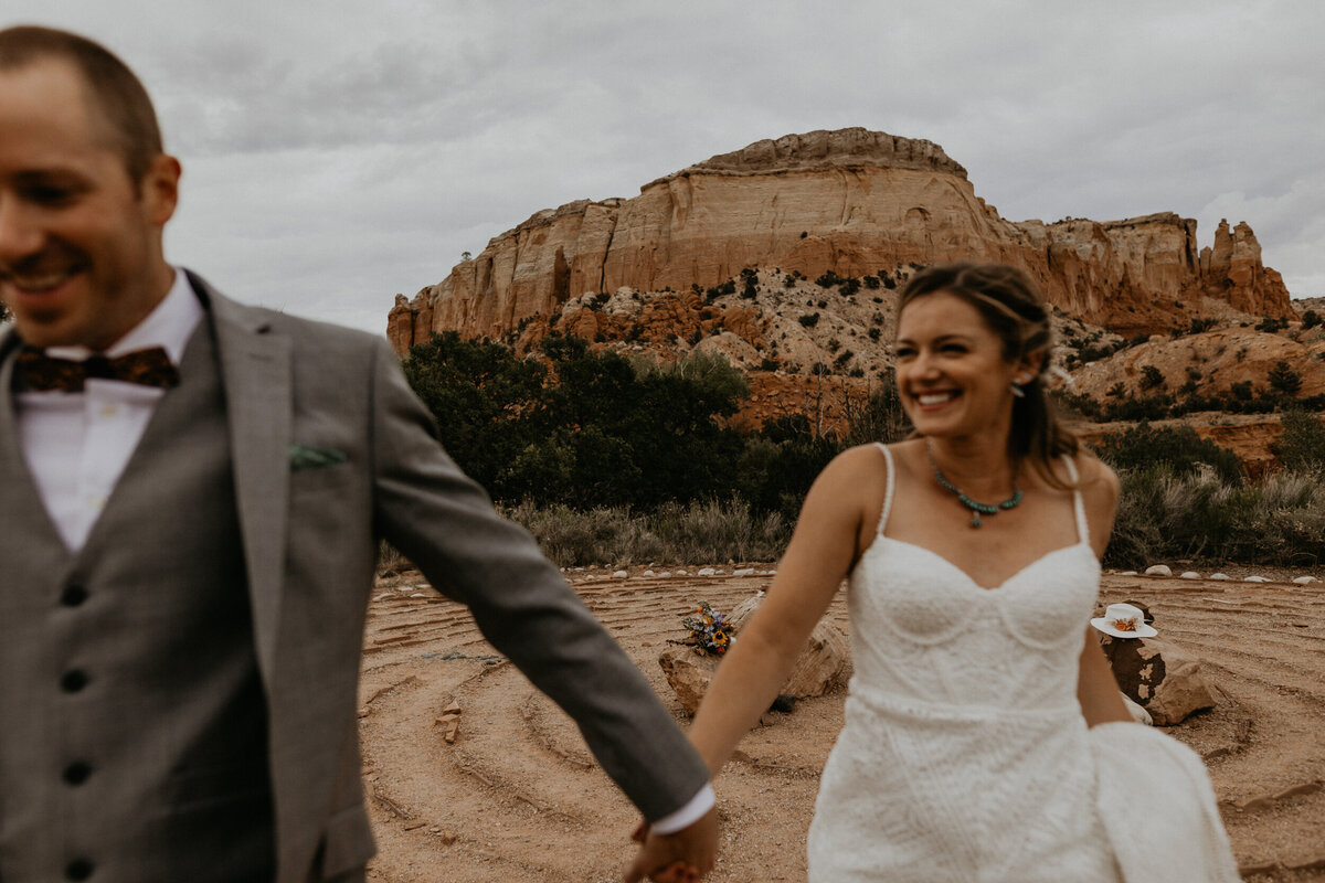 bride and groom running in front of red rocks together
