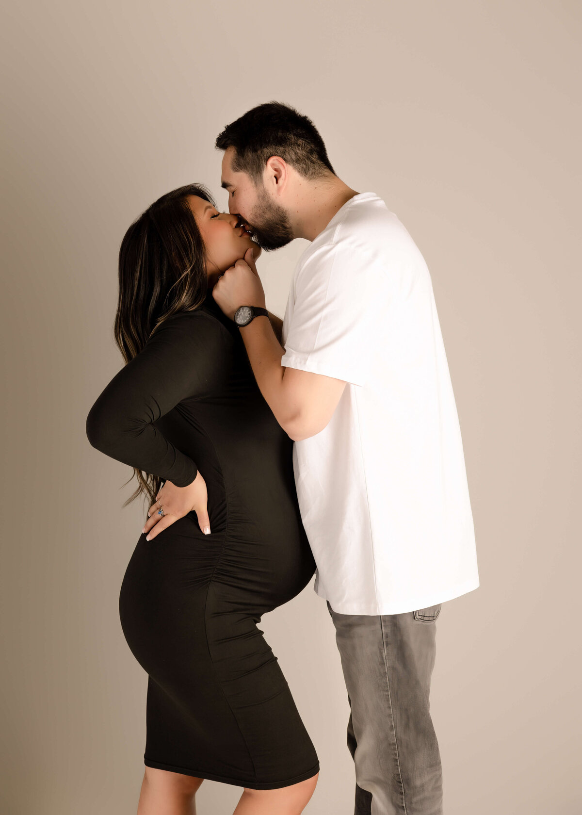 Husband holding wifes chin while giving her a kiss in maternity session in studio by Ashley Nicole Photography.