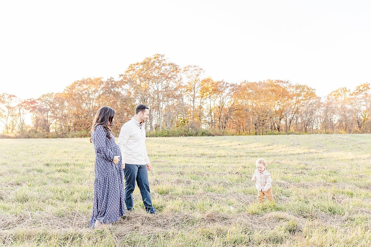 family walks in field  during winter maternity photo session with Sara Sniderman Photography at Heard Farm in Wayland Massachusetts