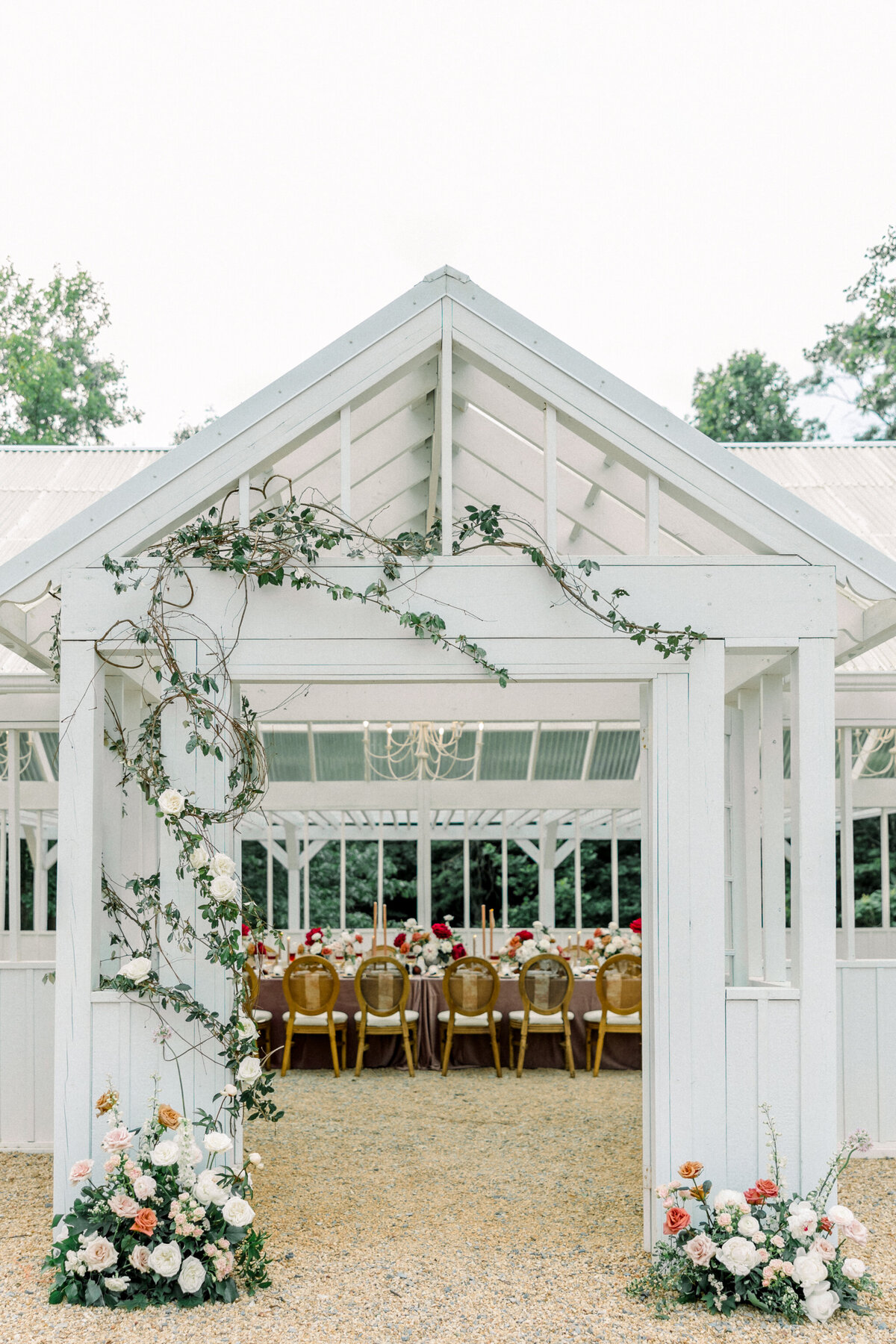 Ivy Rose Barn | Reception decor, consisting of a velvet burgundy cloth-lined table and stunning floral centerpieces and installations through the doorway of a white greenhouse at the Ivy Rose Barn in Virginia. Captured by Virginia wedding photographer, Caitlin Wilcox