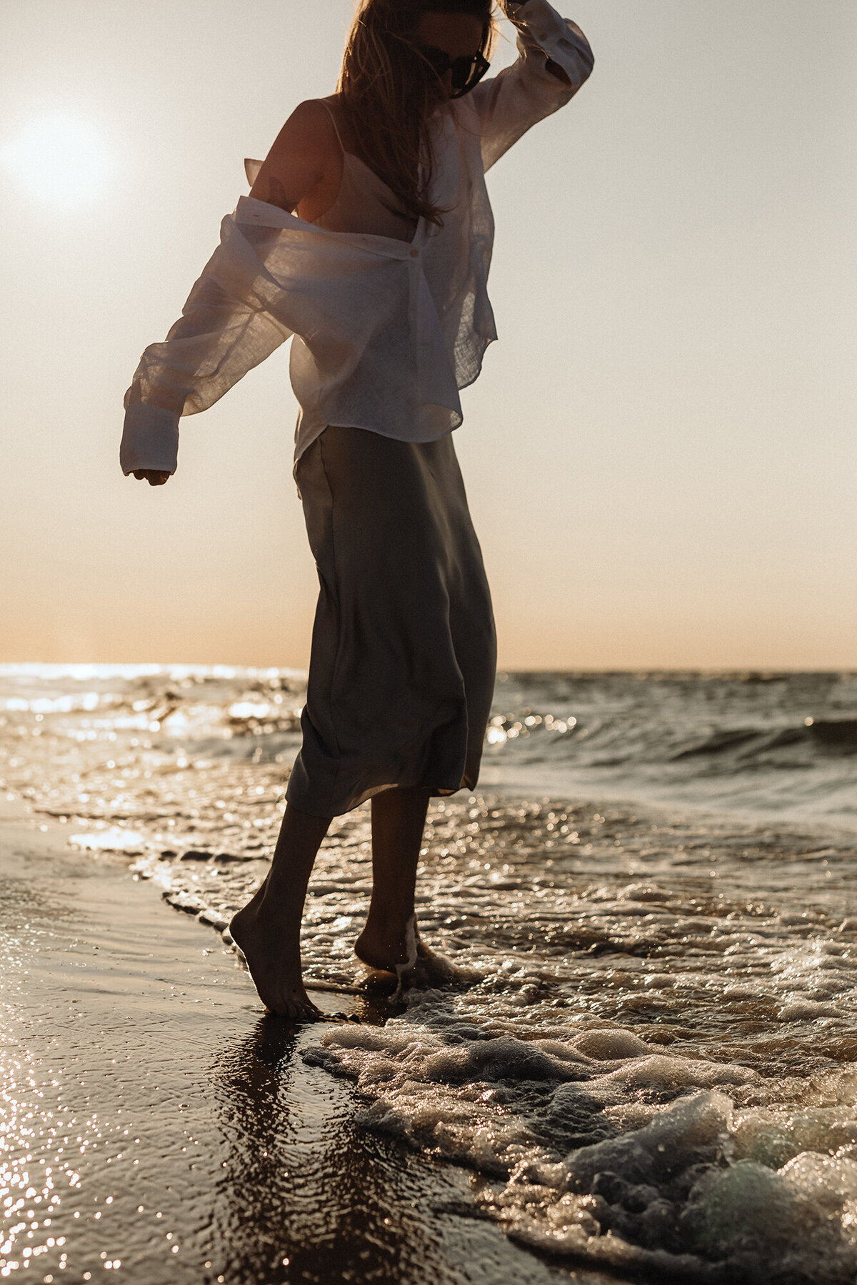 Woman walking through waves at sunset celebrating her Financial Freedom.