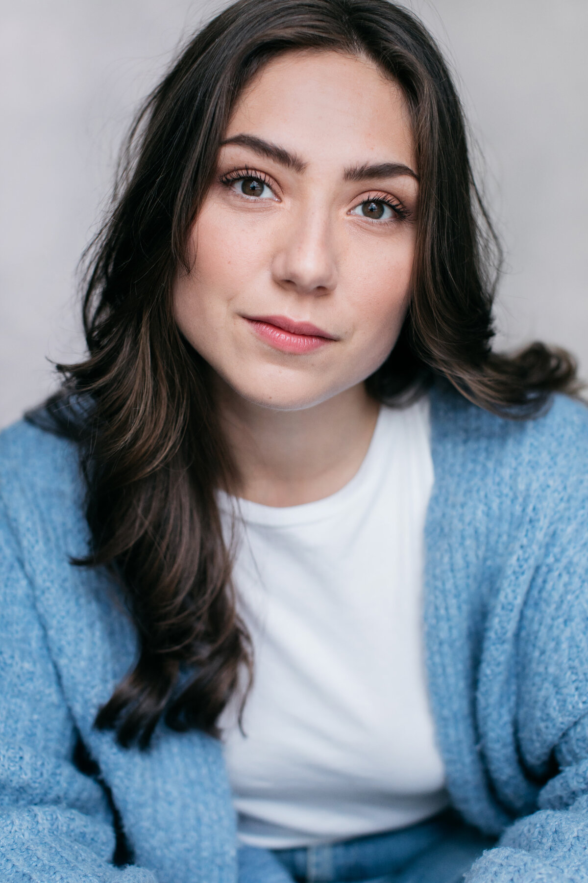 Castingfoto van Pauline Wittebol. Bruinharige vrouw in wit shirt en blauw vest voor grijze achtergrond.