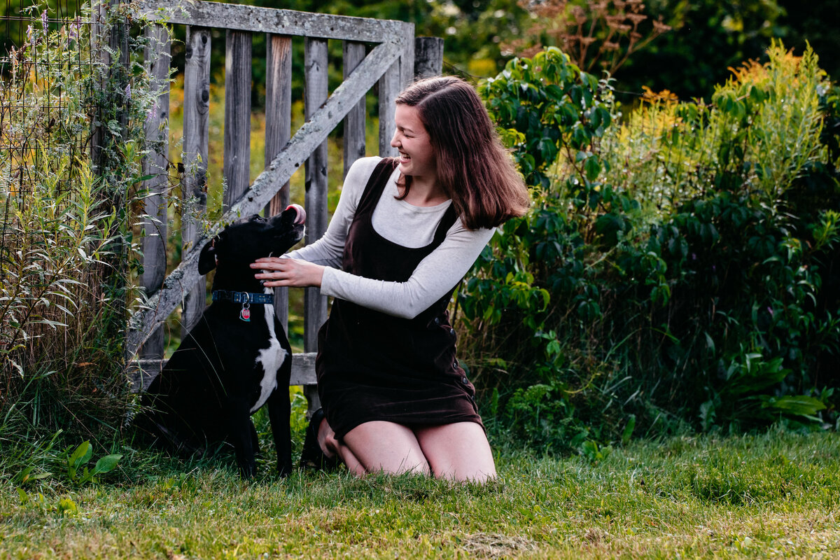 senior girl playing with her black dog in the grass