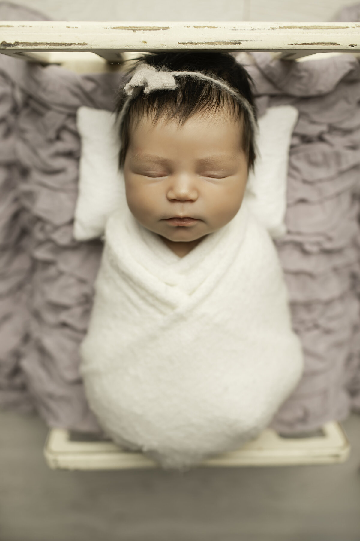 Newborn baby girl peacefully resting on a soft bed adorned with delicate ruffles, creating a dreamy and elegant portrait