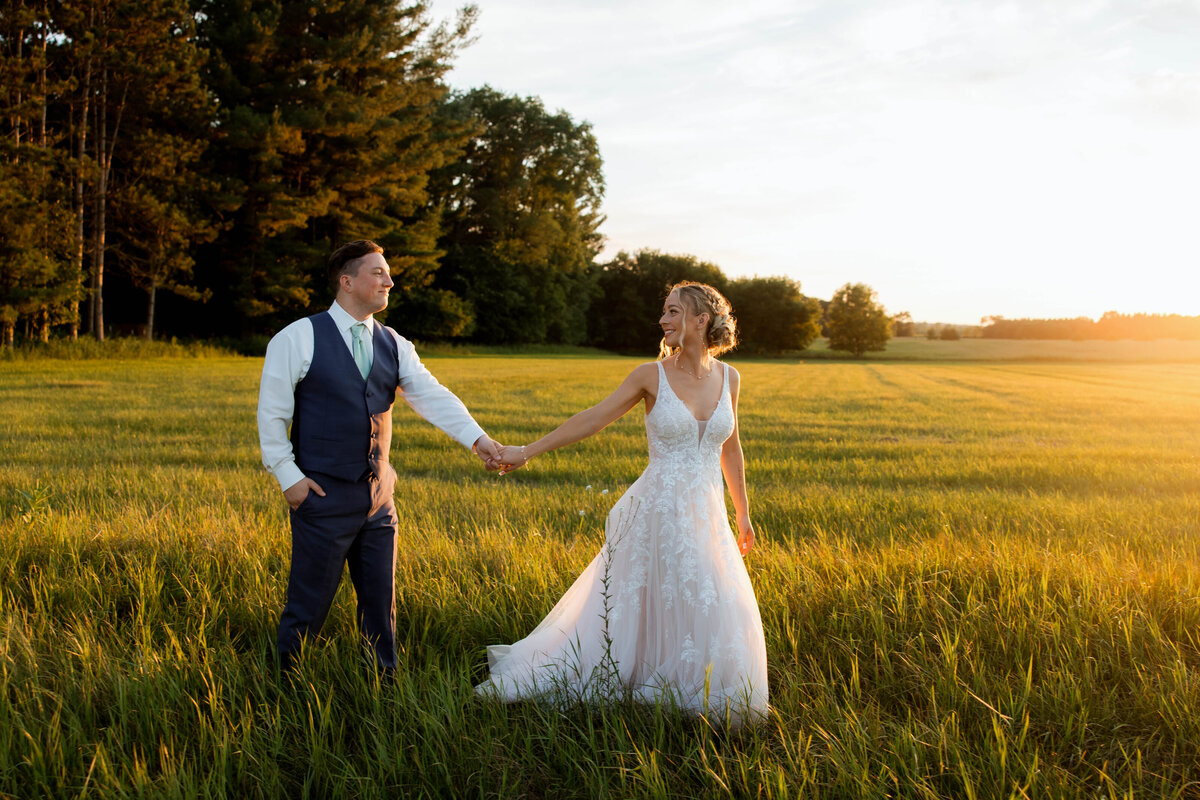 Casual bride and groom walking across MN fields celebrating after booking a professional photography service with Tia Quirk Photography