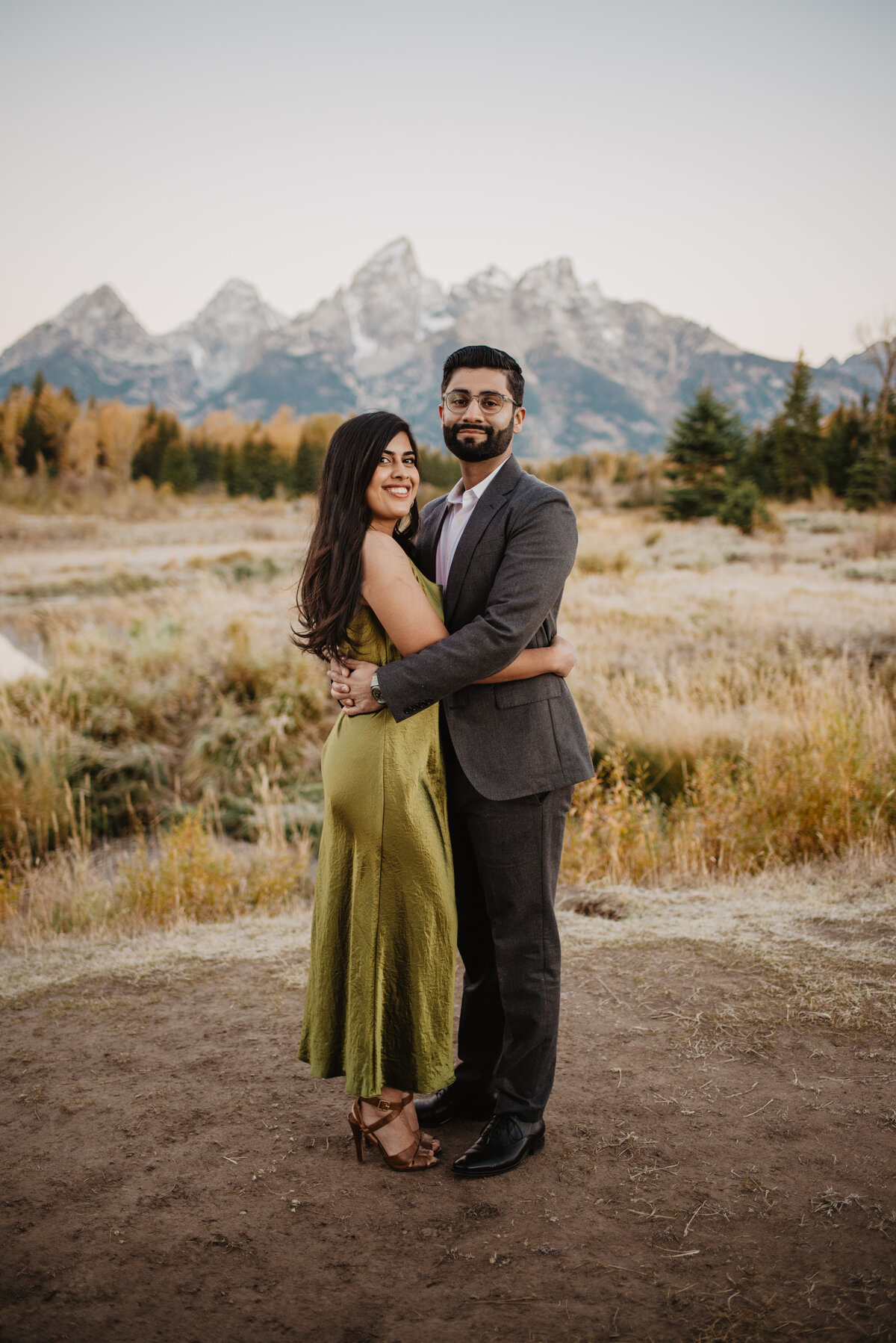 man and woman holding each other at the waist in front of the Grand Tetons during their fall engagement session with photographers in jackson hole