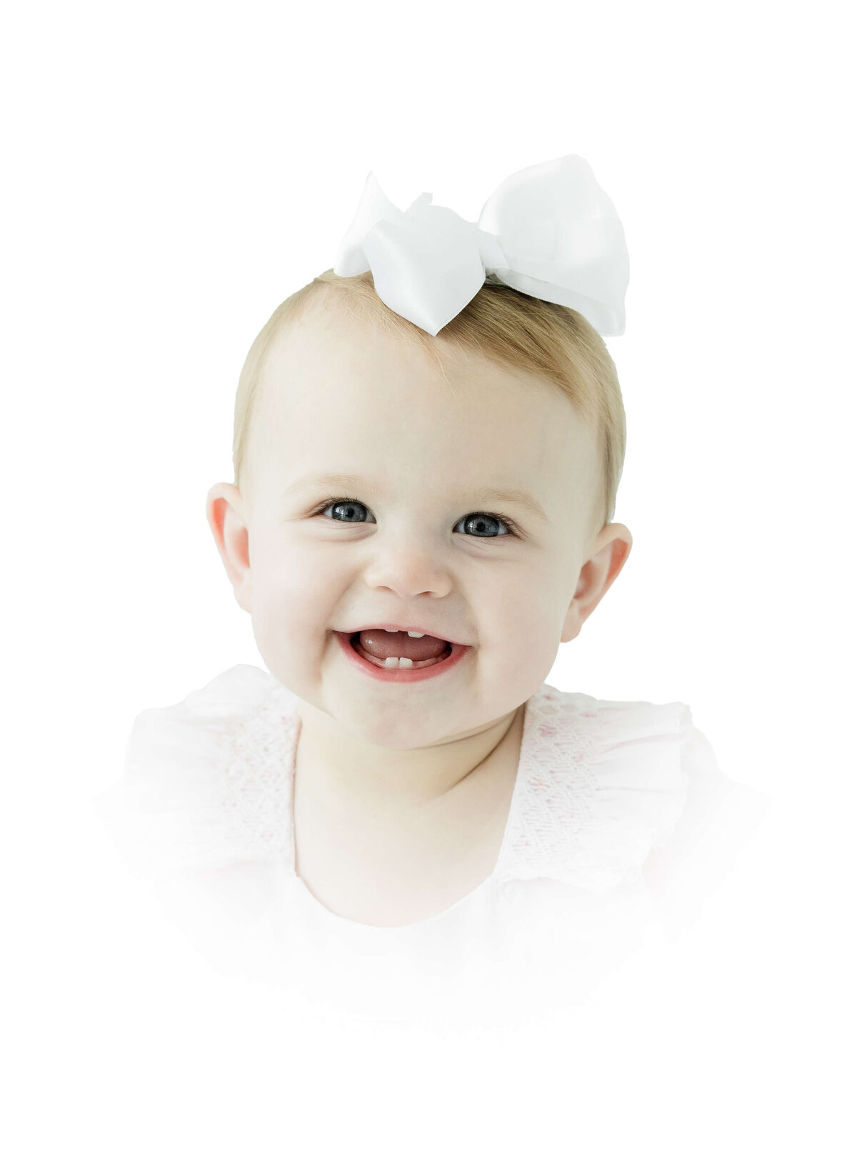Baby sitting and smiling for heirloom photography session in white heirloom outfit with a bow