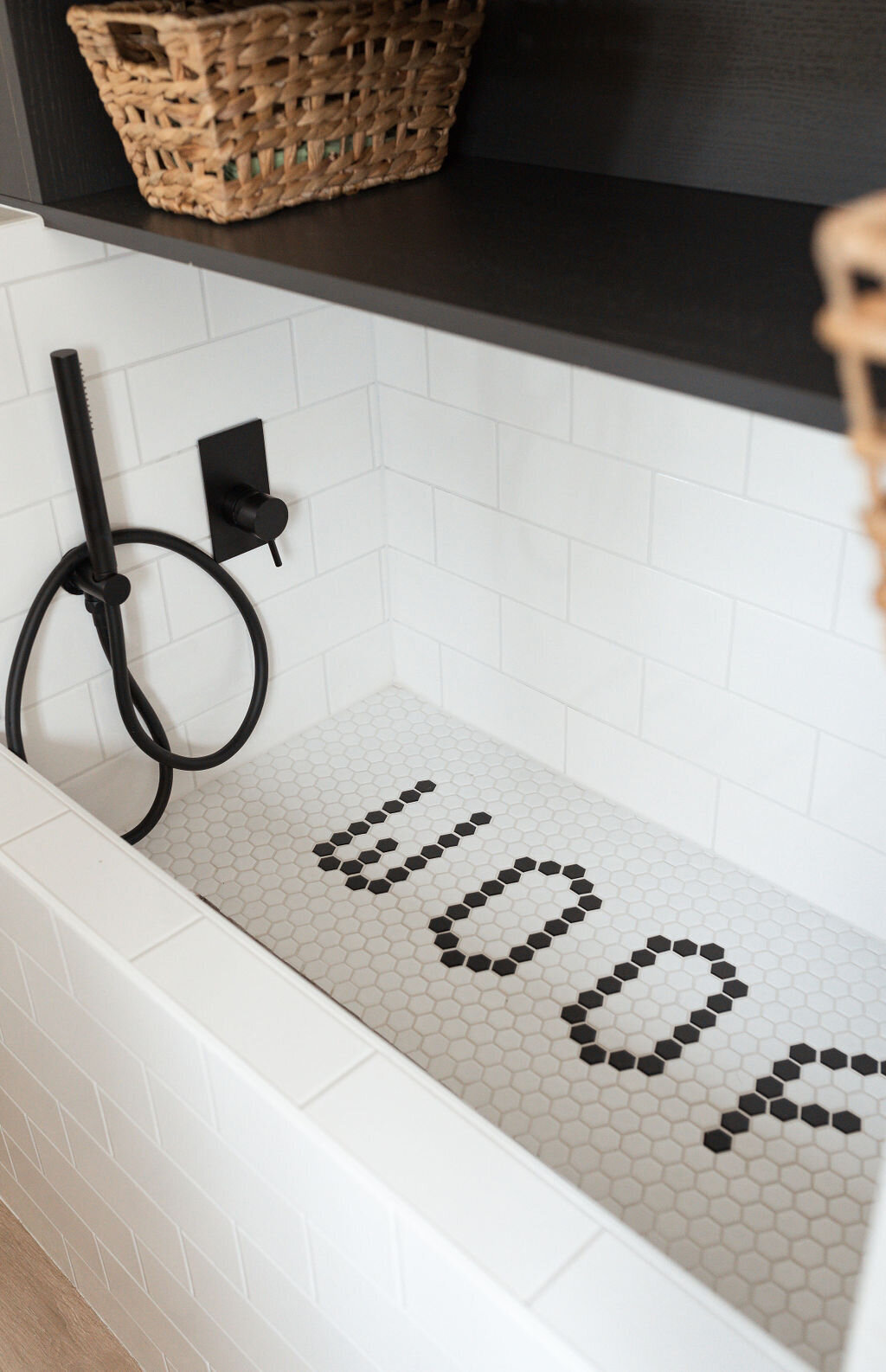 A close look at a modern dog wash room. The washing station is tiled with subway tile and the smaller tiles at the bottom of the tub read ‘woof’. The hardware on the dog shower is black.