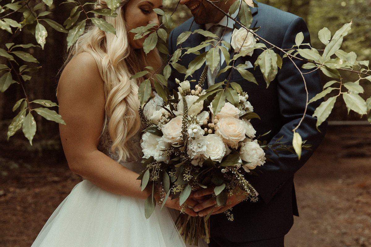 bride and groom holding a white bouquet with  greenery in front of them