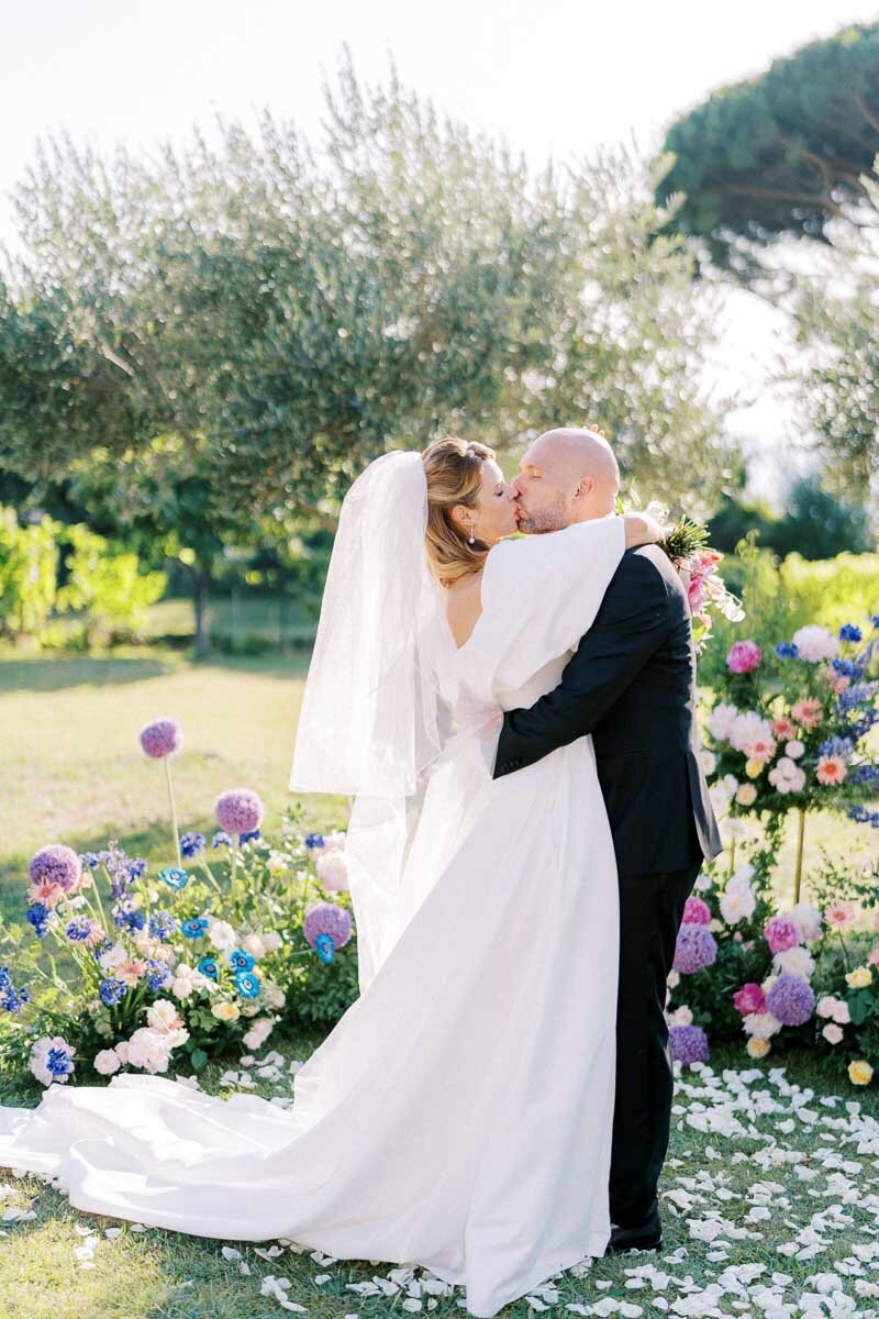 Bride and groom sharing a romantic kiss surrounded by flowers after their outdoor wedding ceremony, captured by a Toronto wedding photographer