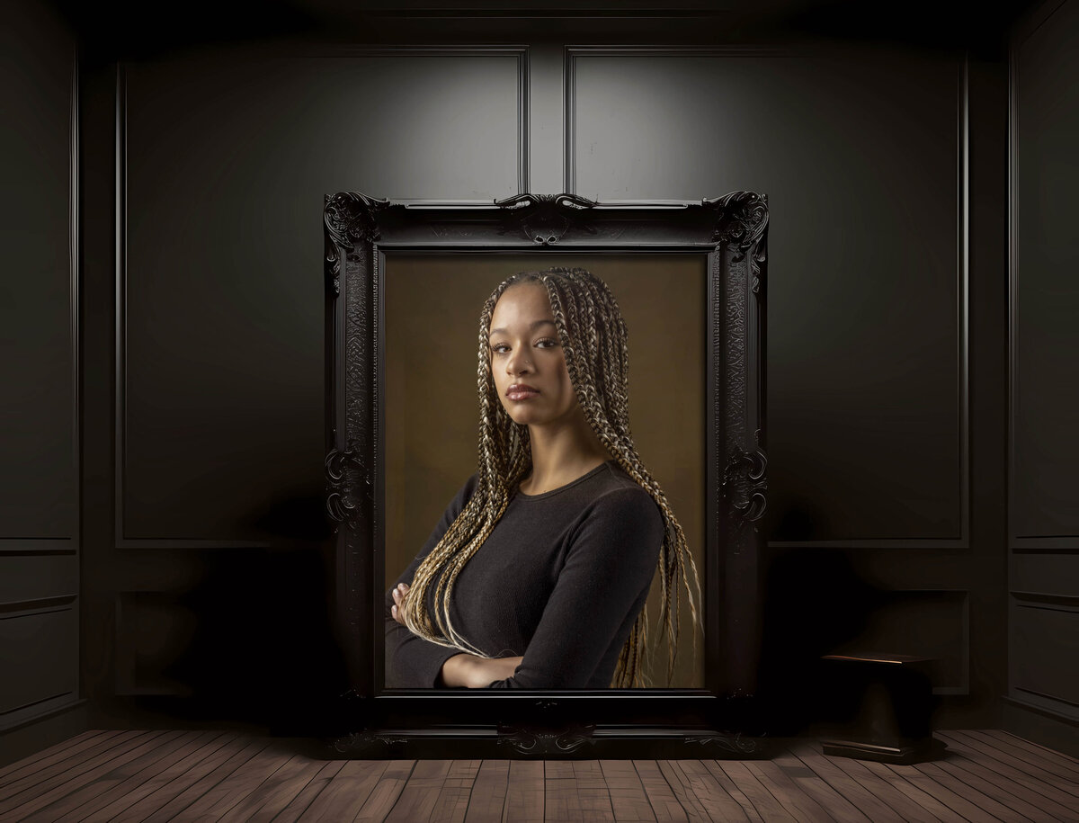 Fine-art style headshot in CT of a young woman with long brown hair wearing a fitted black top, posed with relaxed confidence against a dark studio background, by Rob Faber Photography, expert in headshots in CT and MA.