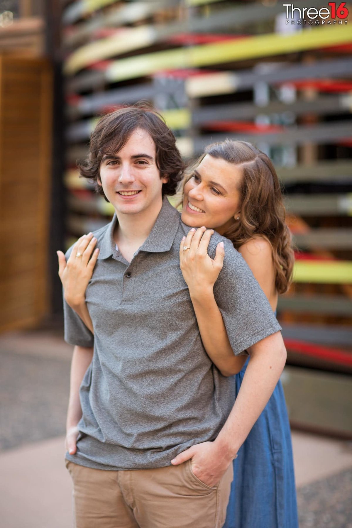 Bride to be holds on to her fiance from behind during photo session