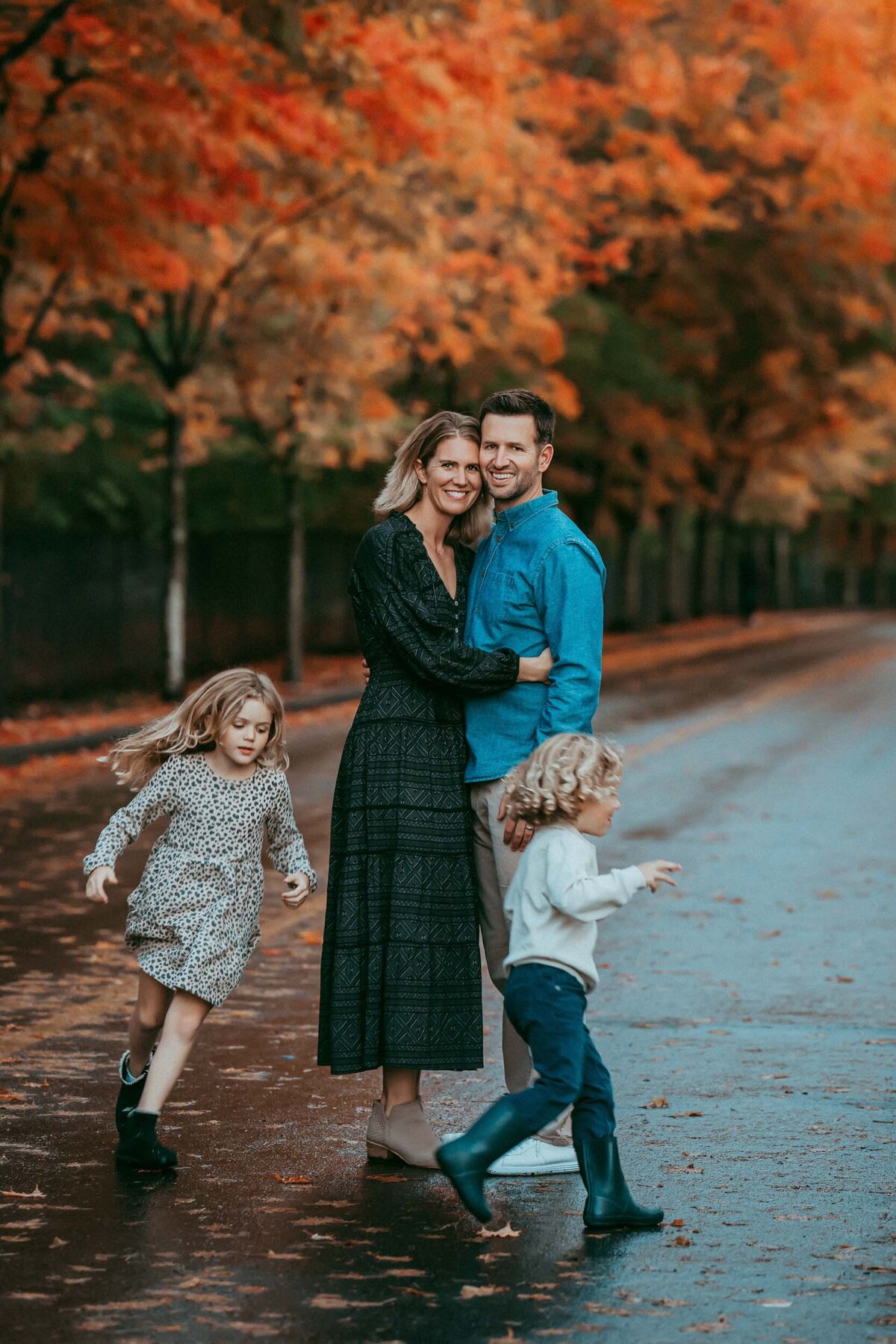 Playful photo of kids running joyfully around their parents, surrounded by colorful fall foliage and golden light.