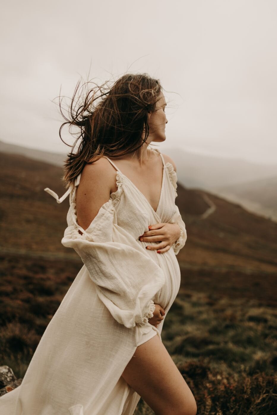 Windswept pregnant woman in a flowing white dress during a scenic Mullingar maternity photoshoot