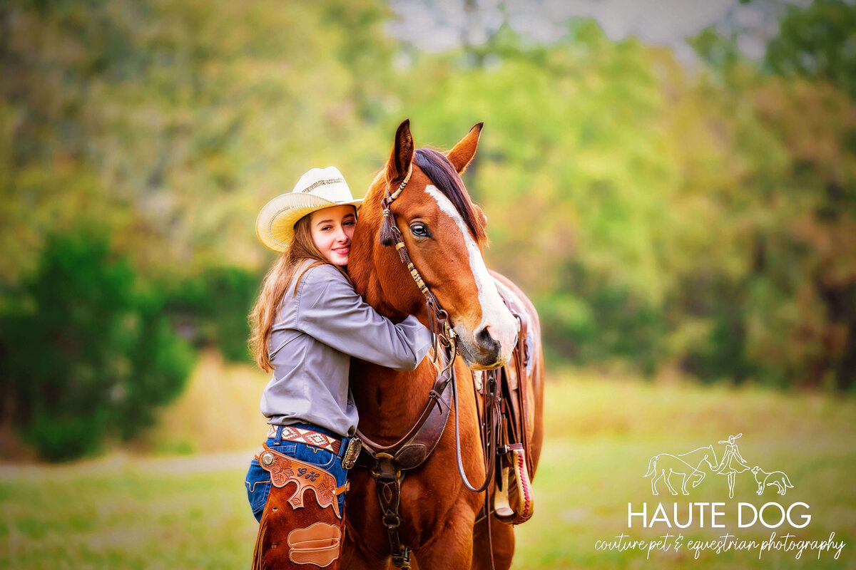 Young female equestrian wearing western attired hugs her paint horse in an open field.