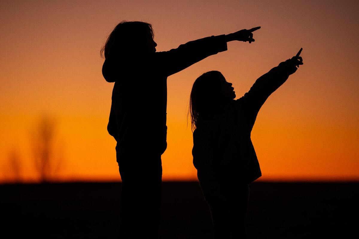 silhouette of two children pointing at the moon
