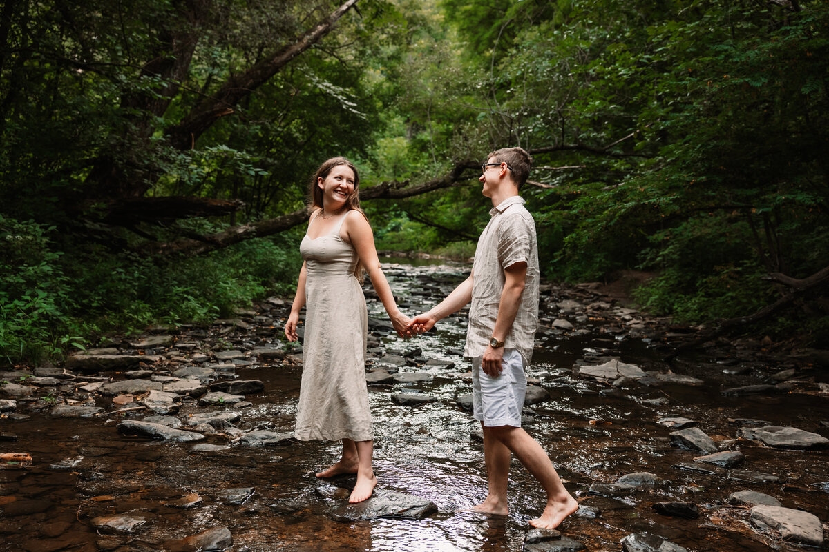 man and woman walk across a stream while holding hands at Devils Lake State Park
