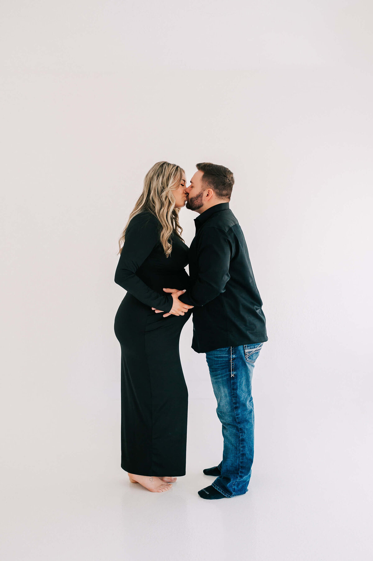 pregnant couple in black outfits kissing during Joplin MO maternity photography session