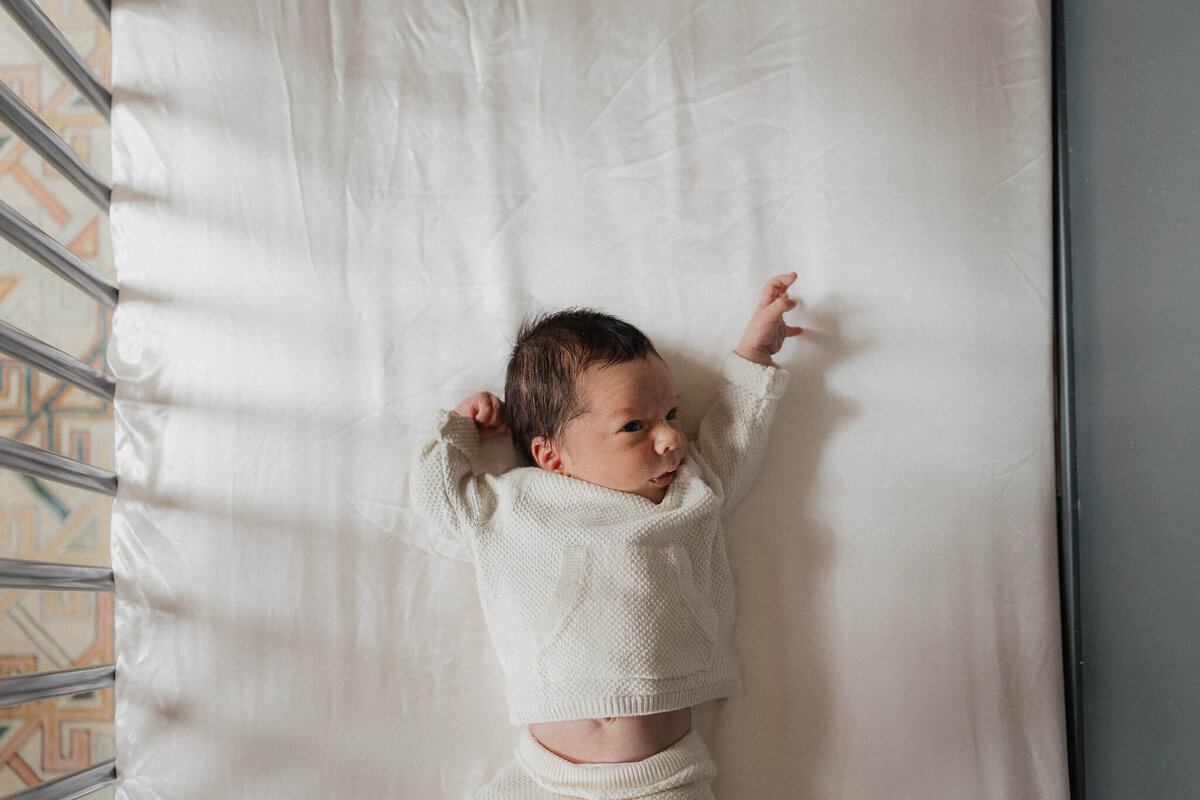 Newborn dressed in white outfit laying in crib during lifestyle photography session in Cleveland.