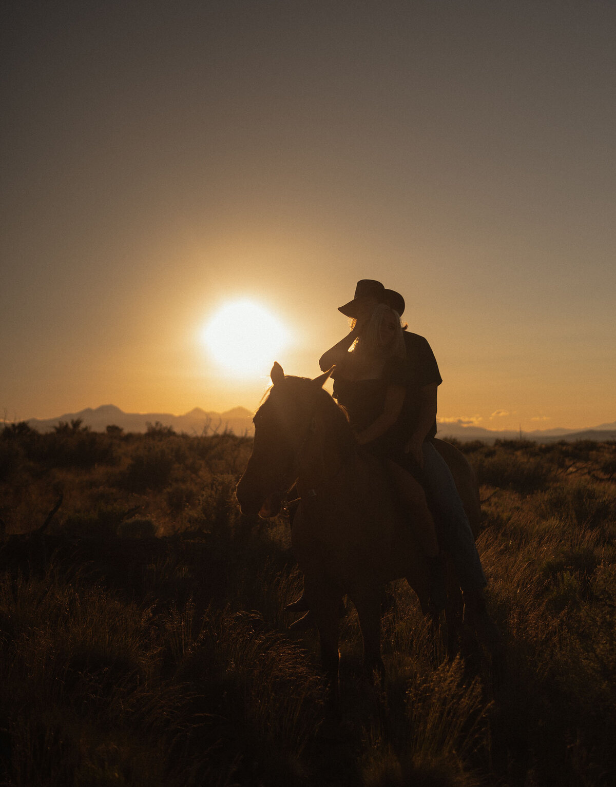engaged couple silhouette riding their horse during a golden hour sunset in the countryside