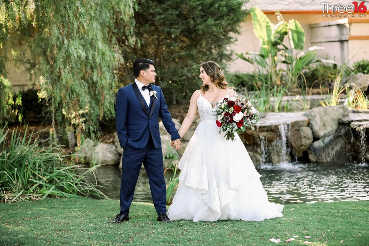 Bride and Groom stand in front of a Coto de Caza Golf & Racquet Club waterfall holding hands and looking into each other's eyes