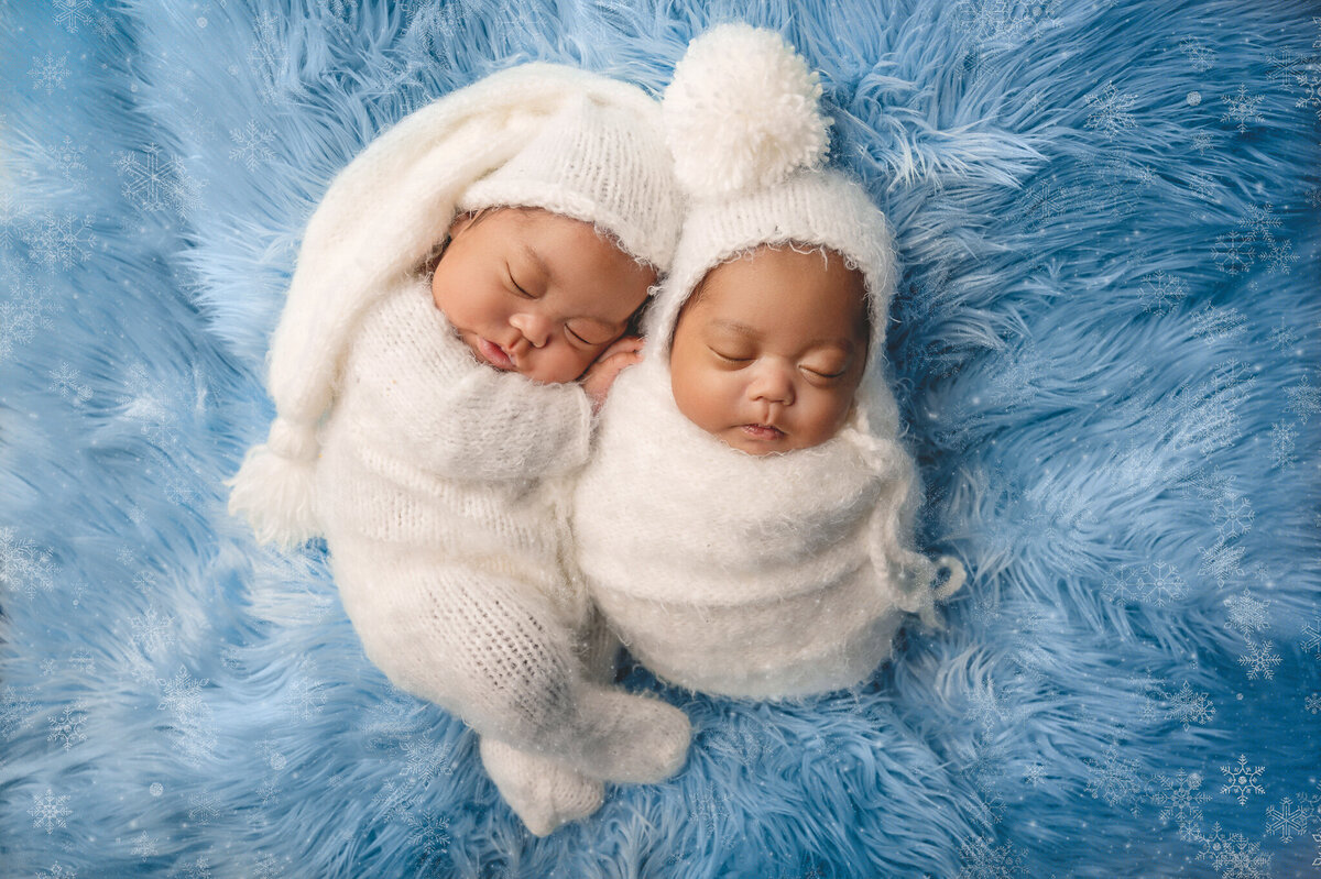 Adorable twins sleeping wearing matching  white cozy outfits on a blue background.