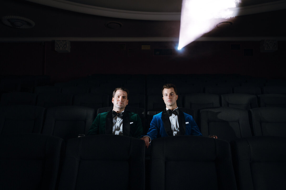 Two grooms sitting on cinema chairs before their wedding.