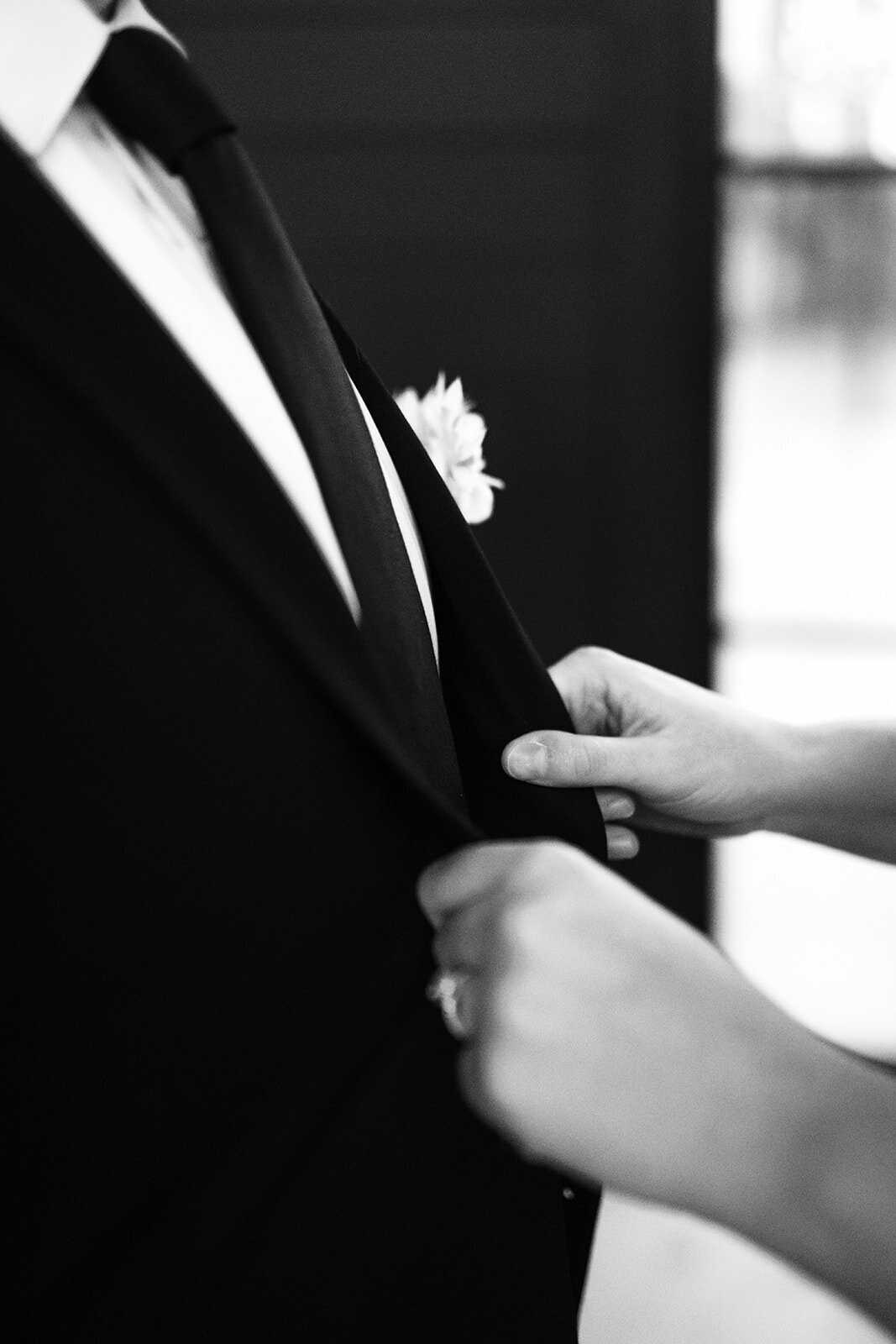 Close of up a groom's tuxedo and a woman's hands holding the lapels during a styled photography shoot.