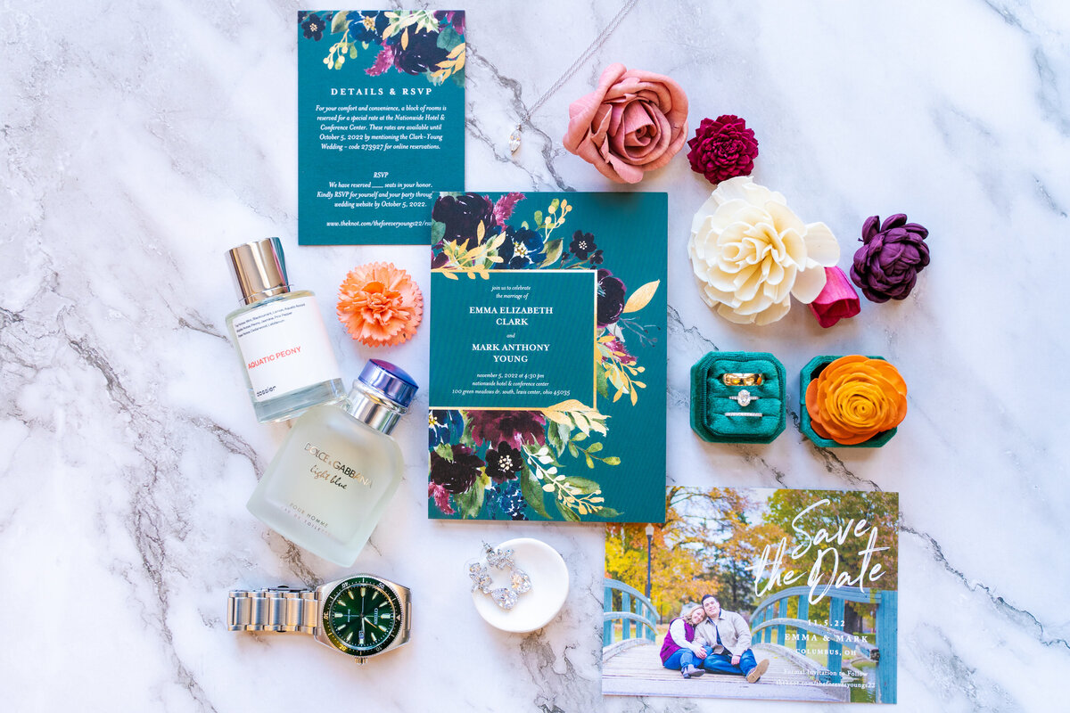 Colorful flat lay with a wedding invitation, save the date, perfume, cologne, watch, jewelry, rings, and Sola Wood Flowers at Nationwide Hotel and Conference Center in Lewis Center, Ohio.