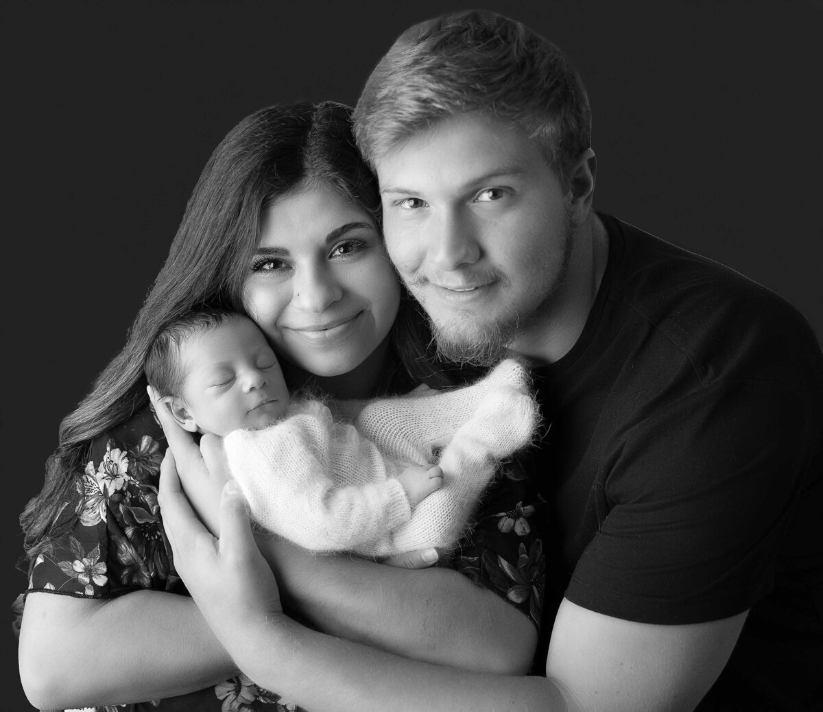 New Mom holds her sleeping baby boy with Dad standing behind her. Mom and dad are smiling at the camera. Captured by Bryn Mwar Philadelphia and Main Line photographer Liza Nicole.