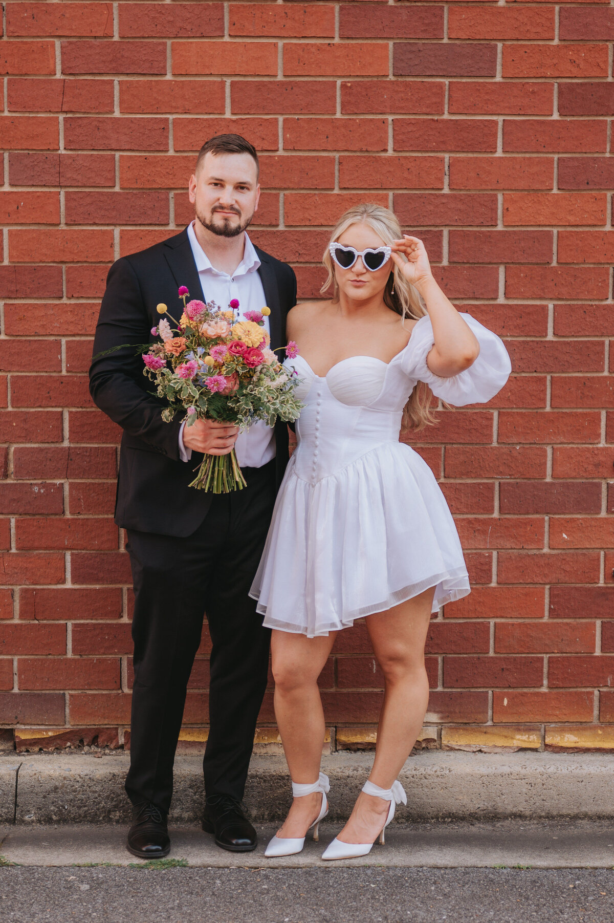 A couple poses in front of a brick wall on their elopement day