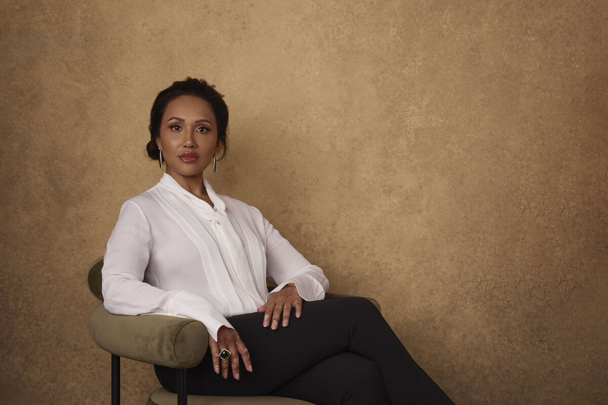 Dr. Rednam sitting in a green chair with glod background in white top and black pants