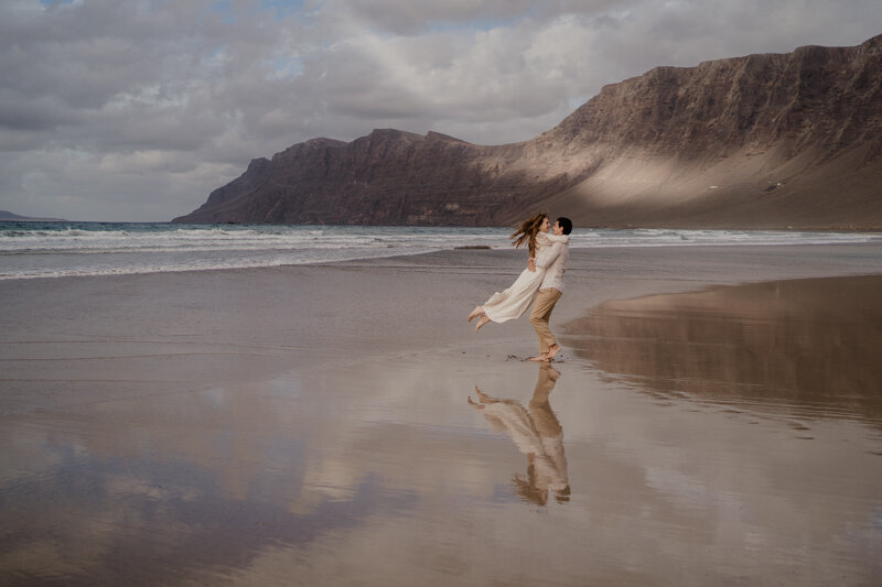 Elopement sur la plage de Famara à Lanzarote, avec un couple dansant au bord de l’eau face aux falaises volcaniques.