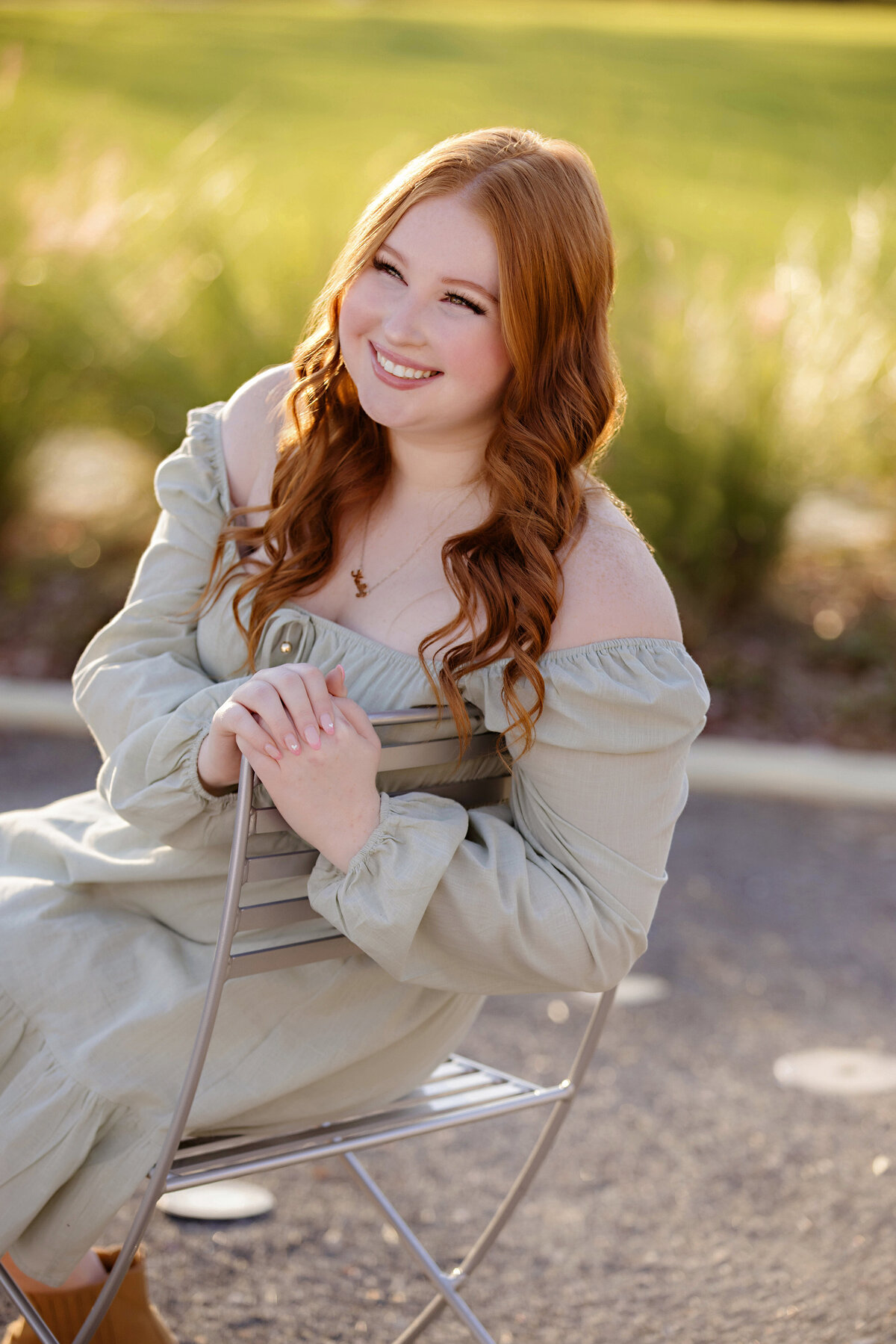 High school senior in green dress sitting in chair surrounded by vibrant greenery and soft golden light
