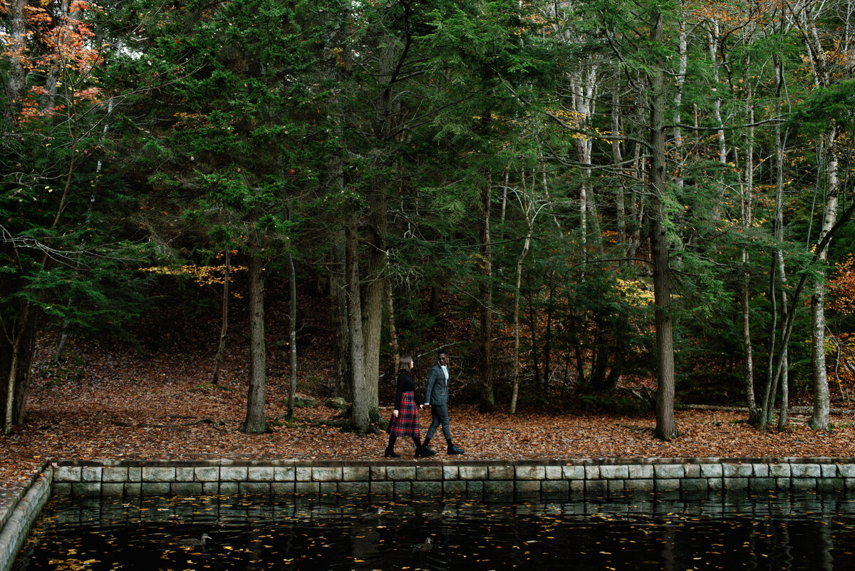 Couple walking through the forest alongside a pond.