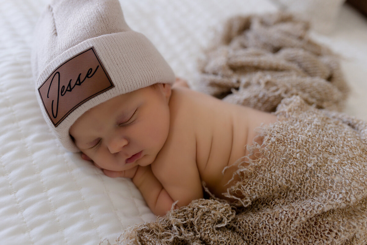 lubbock newborn photographer caaptures infant sleeping on tummy wearing a beanie with name engraved on beanie.