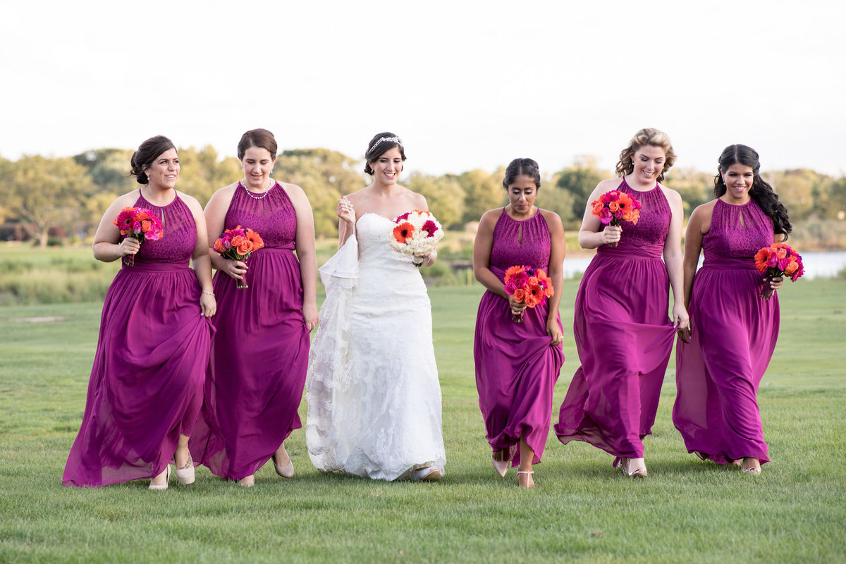 photo of bide with bridesmaids walking on the grass outside wedding reception at Lawrence Yacht and Country Club