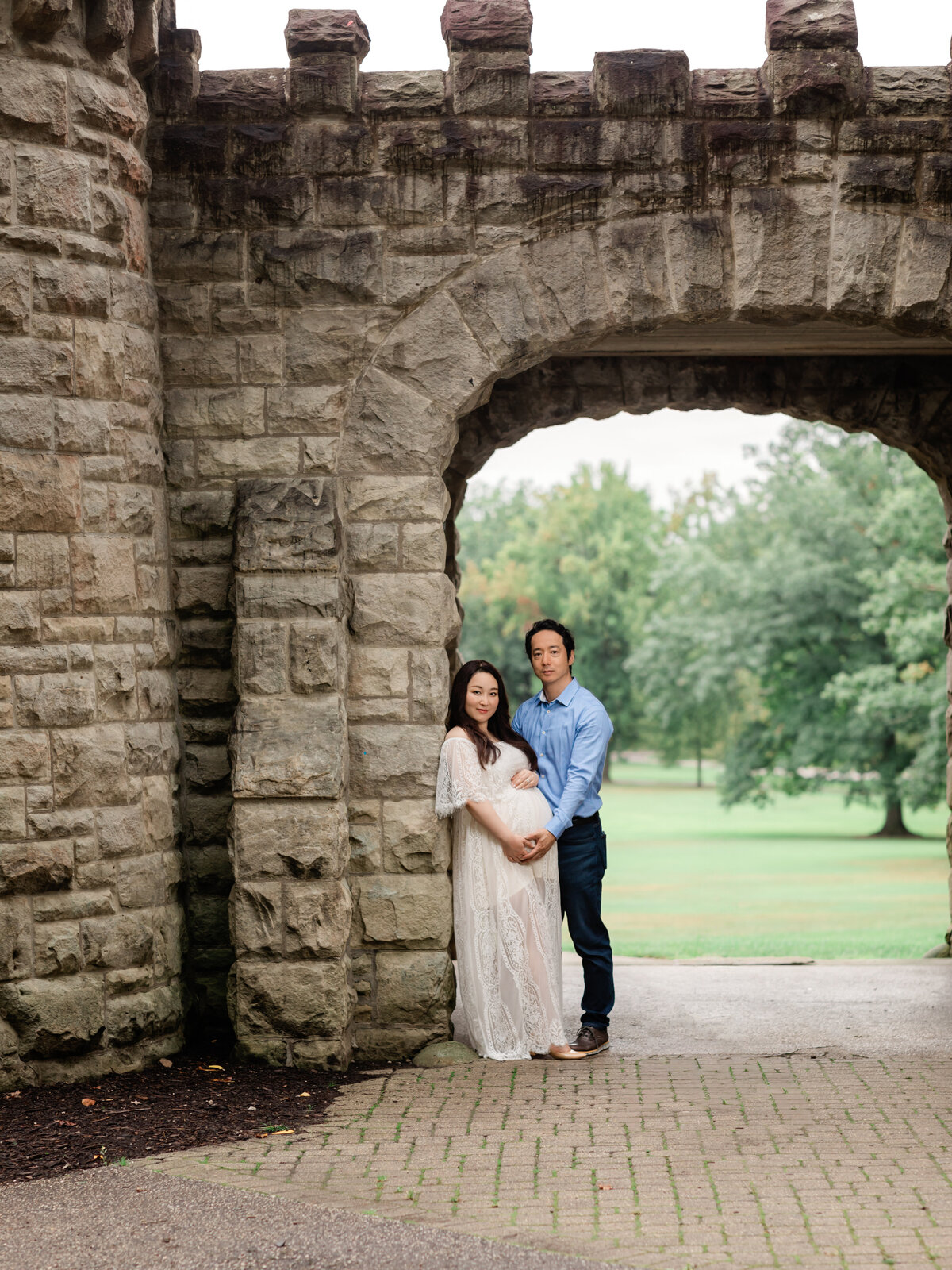 husband and pregnant mother in white lace gown holding belly for maternity portraits 