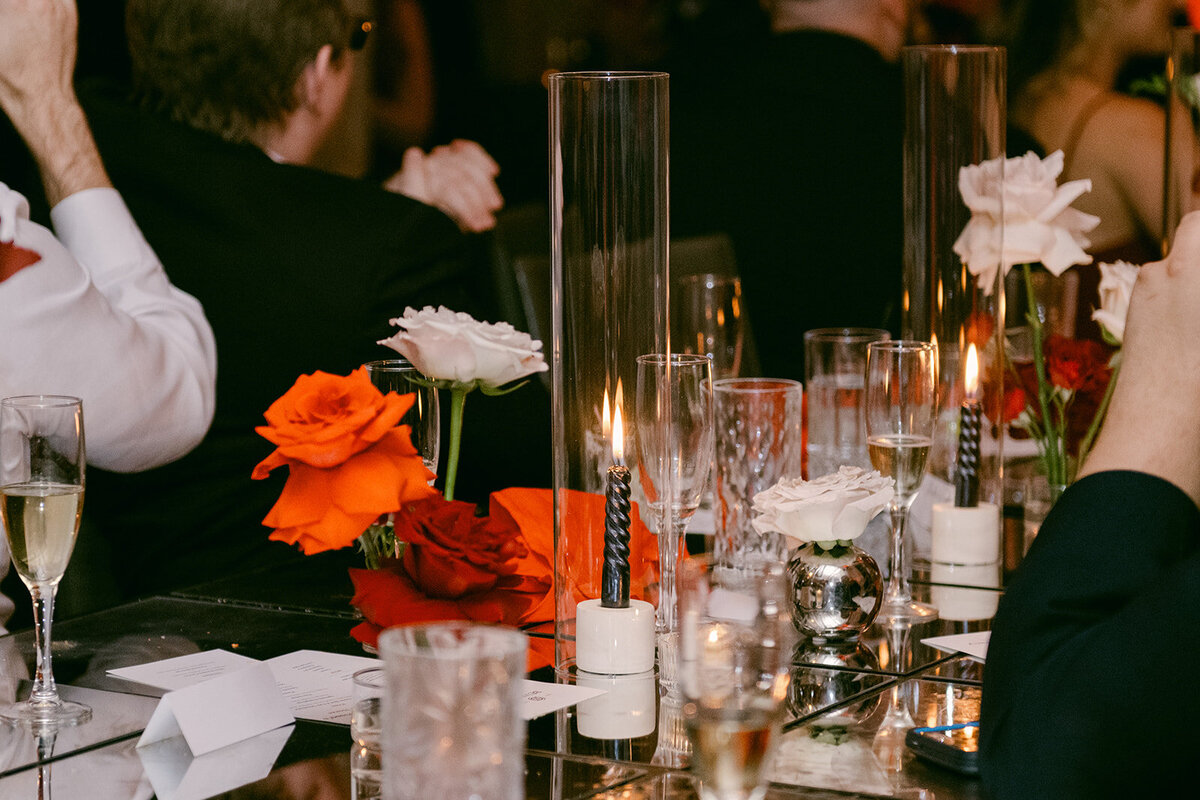 Intimate tablescape detail with red florals and flickering candles at upscale wedding dinner in Texas